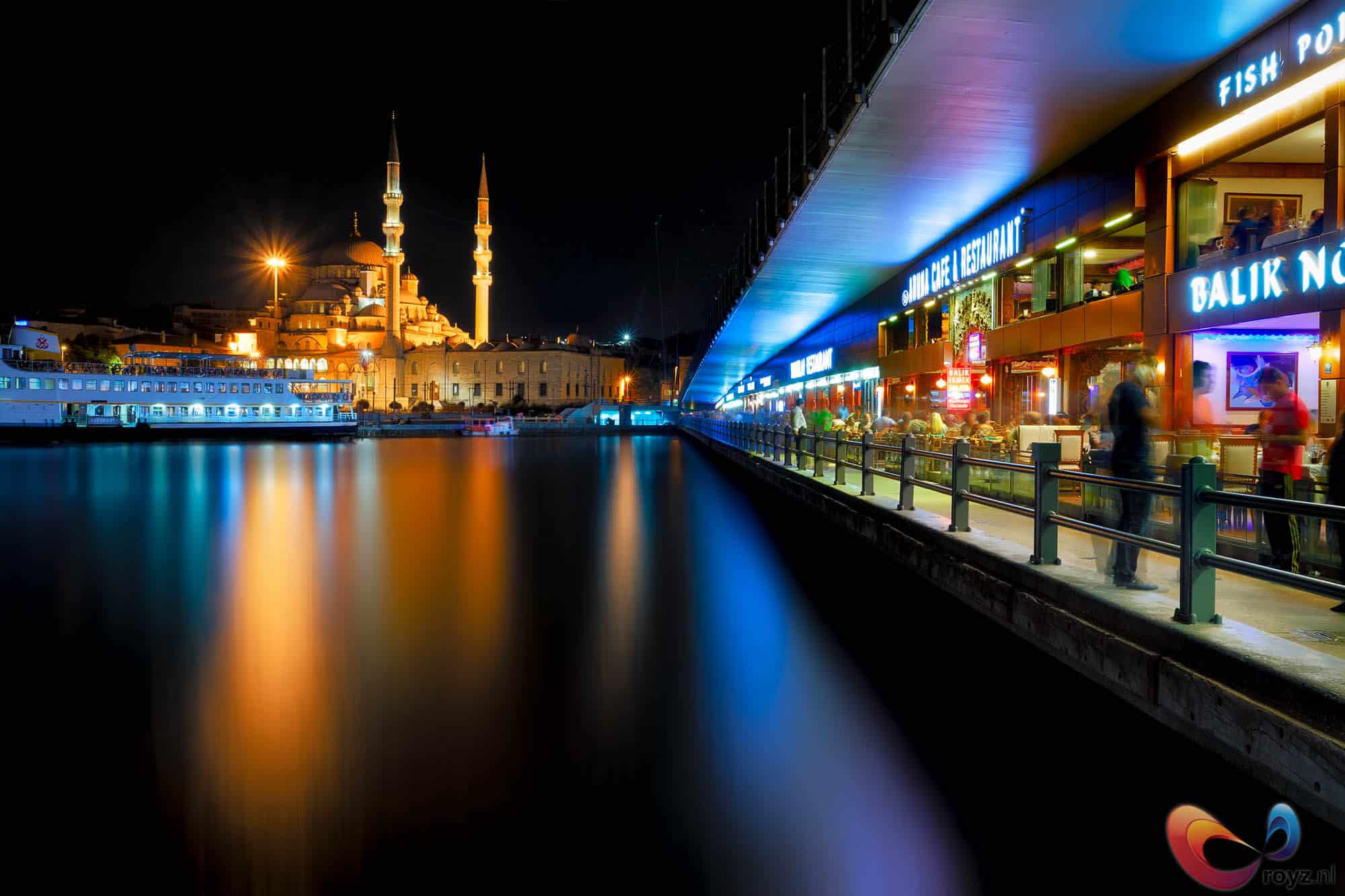 Nachtbeeld Galata-brug in Istanboel: moskee links en blauwe promenade rechts.